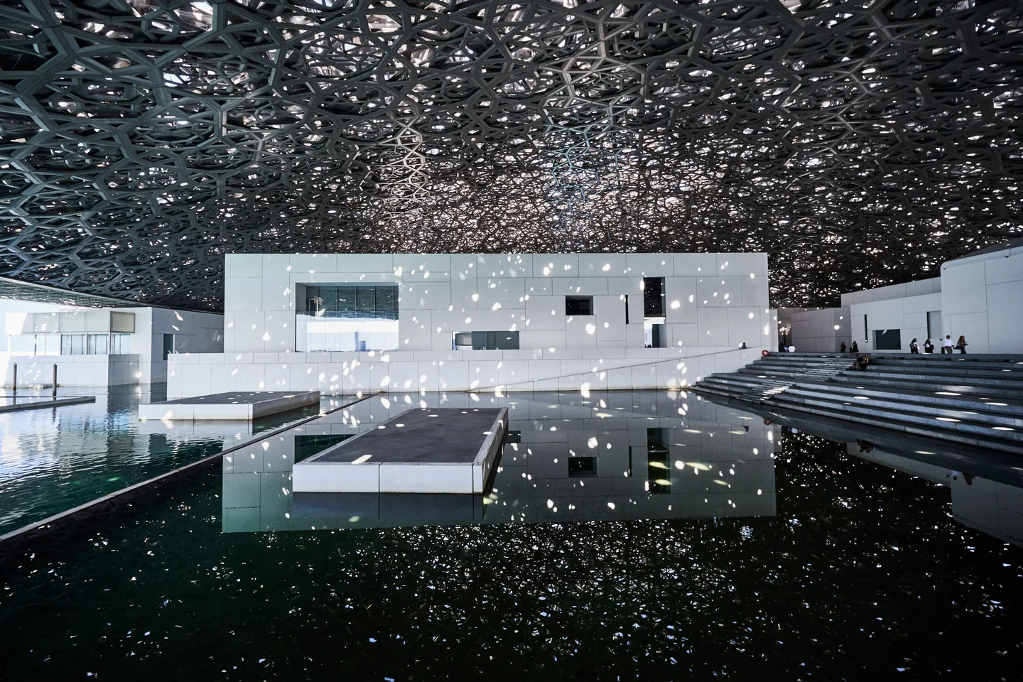 Sunlight scattered across white galleries beneath the geometric dome at Louvre Abu Dhabi